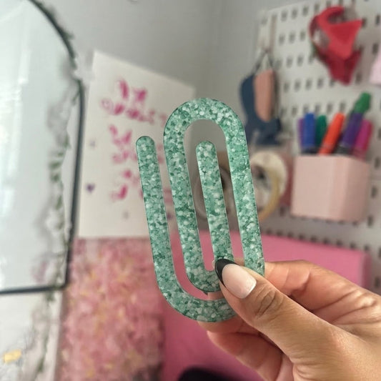 Hand holding a green glittery jumbo paper clip with a blurred background